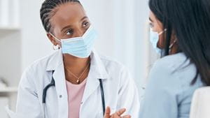 A Black female doctor wearing a mask talks with a female patient who is also wearing a mask