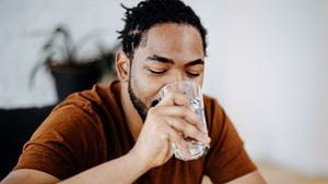 A Black man drinking a clear liquid from a clear glass
