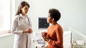 A White female doctor talks with a Black female patient in an office setting