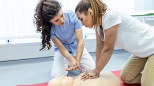 Two women perform CPR on a mannequin
