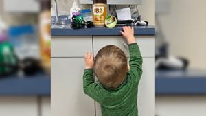 Jackson, a toddler, reaches up toward a countertop in a pediatric office