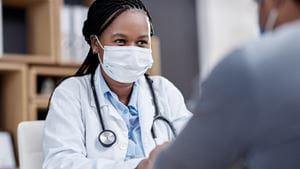 A Black female doctor wearing a mask speaks to a patient