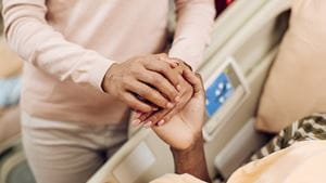 A family member and patient hold hands in a hospital bed