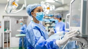 A Black female surgeon looks at a computer in an operating room