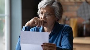 An older White woman reads a letter with a worried expression on her face