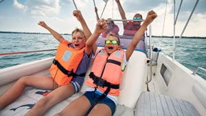 Two children and two adults wearing life jackets are excited riding on a boat