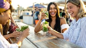 Young women celebrating at beach chiringuito, focus on brunette woman with toothy smile