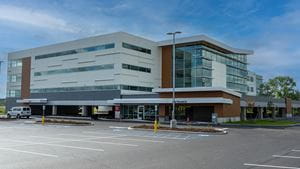 An external photo of the Batavia Medical Campus - a modern building that is mostly grey and brown with large windows set against a bright blue sky