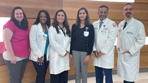 The Cardiology-Oncology team at Sands-Constellation Heart Institute gathered in front of a wood panel background