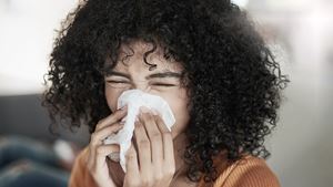 Shot of a young woman blowing her nose with a tissue at home