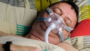 Middle aged overweight man wears a CPAP to help him sleep due to sleep apnea