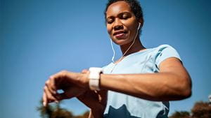 A Black woman looks at her smartwatch after exercising outside with headphones in