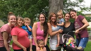 A group of six white women and 4 young children smiling in a suburban backyard with trees in the background