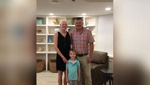 A woman bald from cancer treatment smiles for a family photo with her husband and young son with white bookshelves behind them