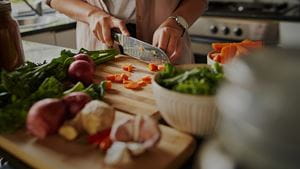 Closeup of young female hands chopping fresh vegetables on chopping board while in modern kitchen