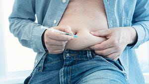 A man with an open button down shirt injecting a weight loss drug into the fat of his stomach