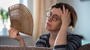 Exhausted middle aged woman waving her fan, suffering from menopausal symptoms, experiencing hot flush