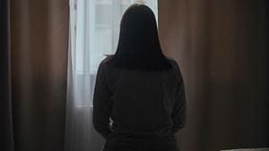Silhouette of a young woman in pajamas against the background of a window at home on a bed with seasonal affective disorder or depression. The concept of winter depression due to lack of sunlight