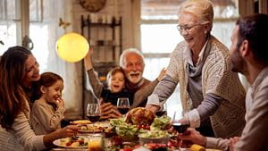 Happy mature woman serving food to her family during Thanksgiving meal at dining table