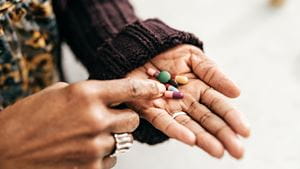 Black woman in brown sweater holds vitamins and supplements in palm of her hand