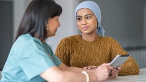 Young woman wearing head wrap talks with female doctor at table