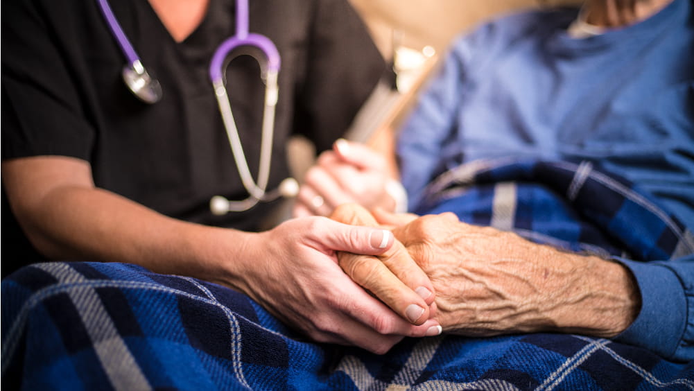 A medical professional holds the hand of an elderly patient