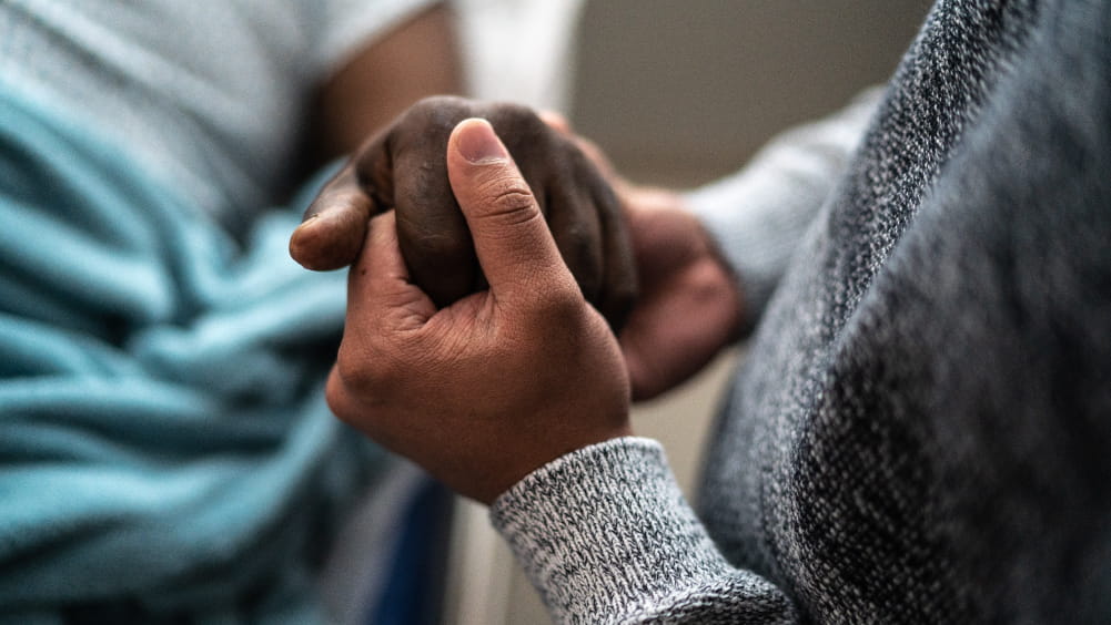 A family member holds the hand of a hospice patient