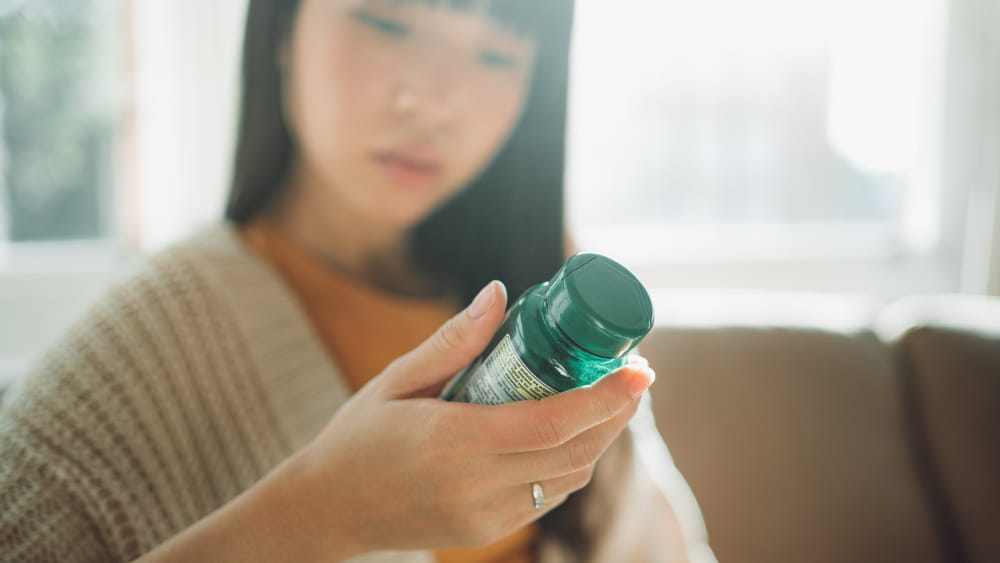 An Asian woman looks at a green medicine bottle