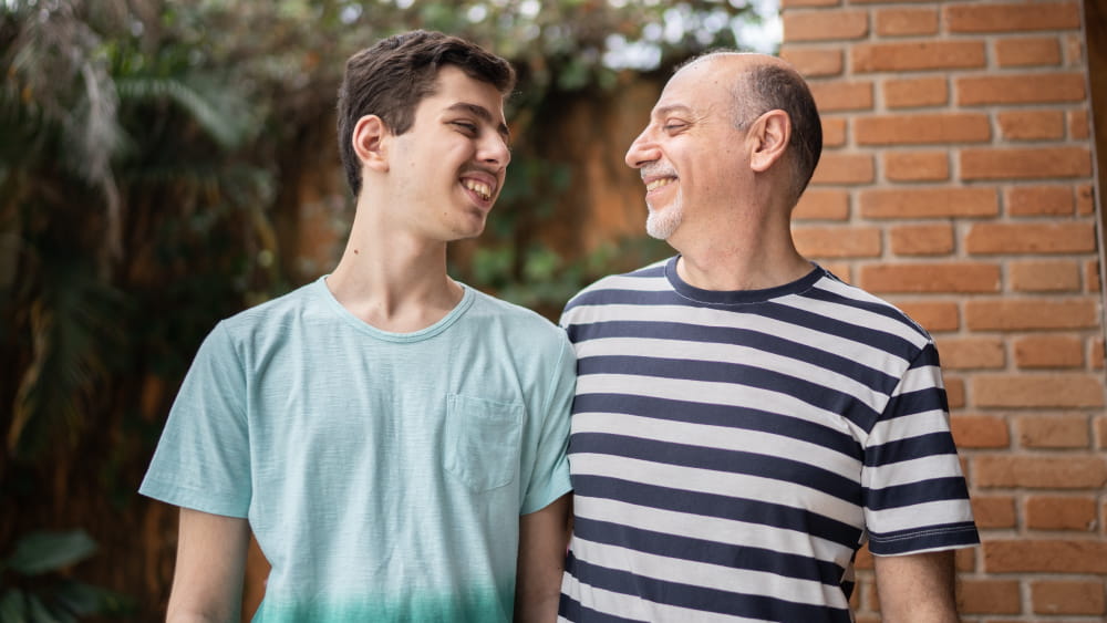 A white teenage boy and a white middle-aged man smile at one another