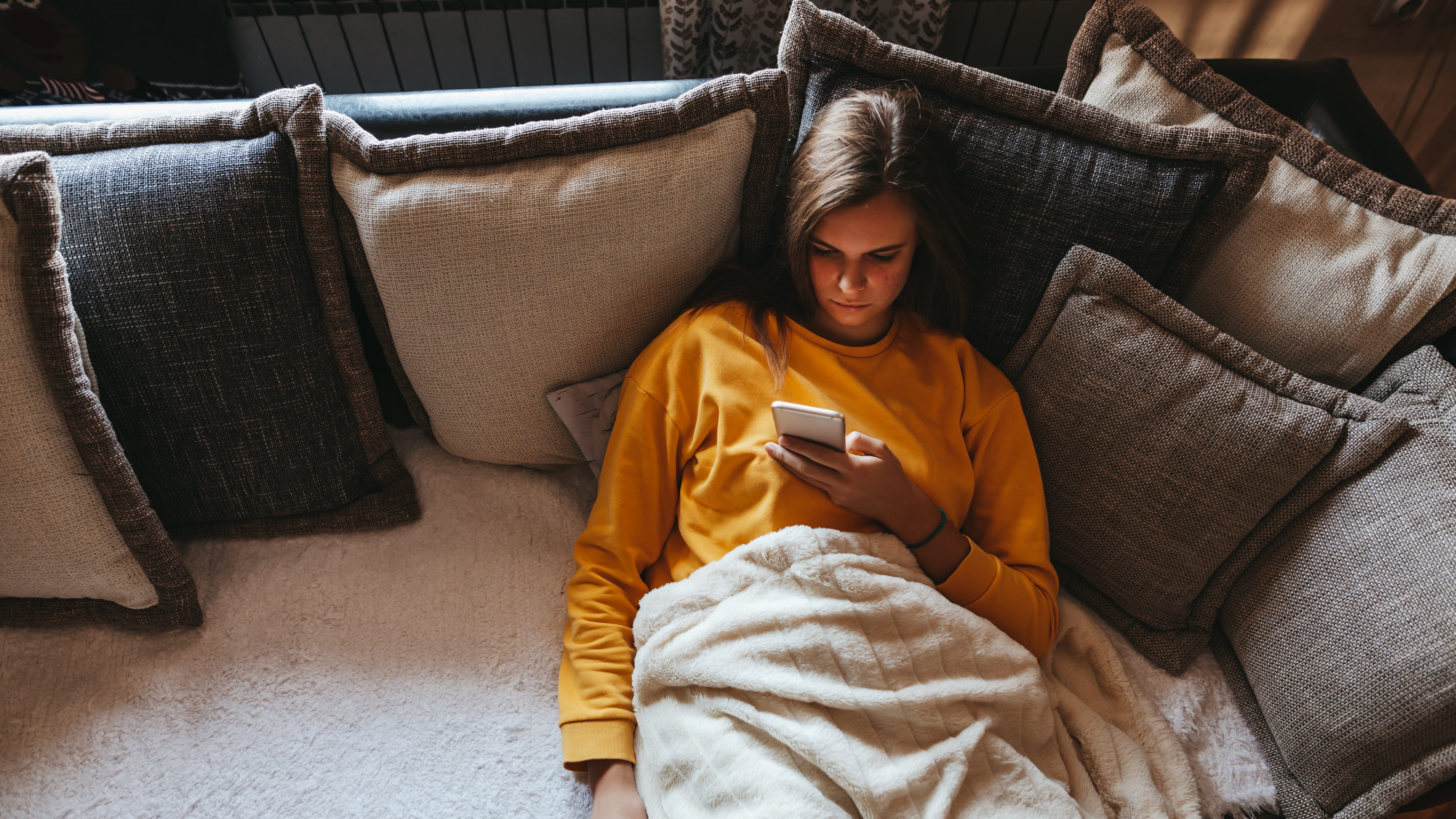 A young woman on a couch scrolling on her smartphone