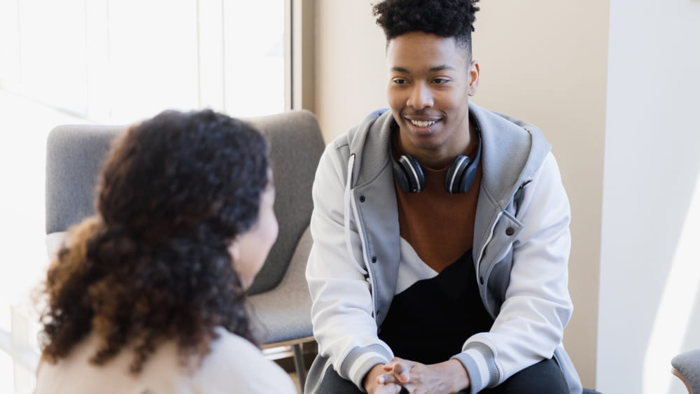 A young Black male teenager talks with a Black female therapist